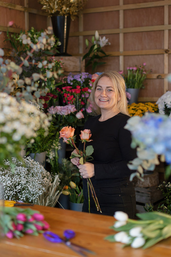 Woman holding flowers in a floral shop with various flower arrangements around her.