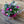 Load image into Gallery viewer, A vibrant mixed flower bouquet wrapped in clear cellophane and bright pink tissue paper, resting on a wooden surface against a wooden plank wall. The bouquet features pink roses, pink tulips, purple flowers, pink gerbera daisies, and green foliage.
